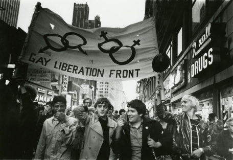 Fotografía de la primera manifestación del orgullo LGBT donde se ve a 4 chicos y detrás una pancarta del Gay Liberation Front