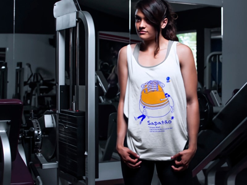 Photograph of a girl in a gym showing a shirt with the Sapatão drawing.