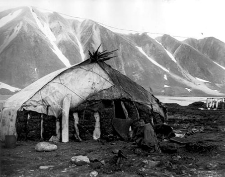 La cada Inuit es una choza fabricada con piedra, turba y piel. Al fondo grandes montañas. Fotografía en blanco y negro.