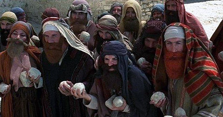 Frame from the film "The life of Brian" in which the mob, preceded by women disguised as man, is getting ready to stone somebody. In the present day, people are still being killed in the same way.