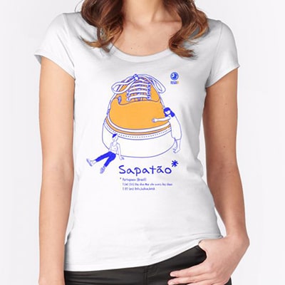Fotografía en primer plano de una camiseta blanca que lleva una chica con el diseño Sapatão, una gran zapatilla con dos pequeñas chicas alrededor, con el argot en grandes letras en su parte inferior. Dibujado en colores azul y naranja.